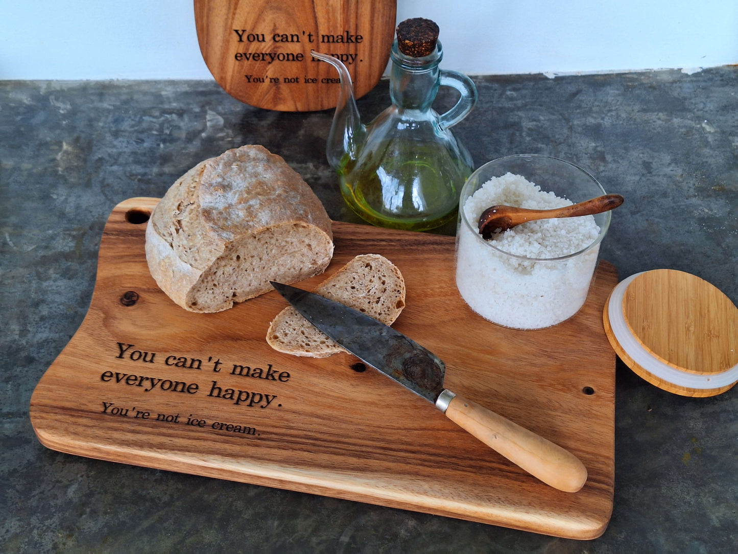 wooden cutting board engraved with humor quote, and displayed with bread and olive oil